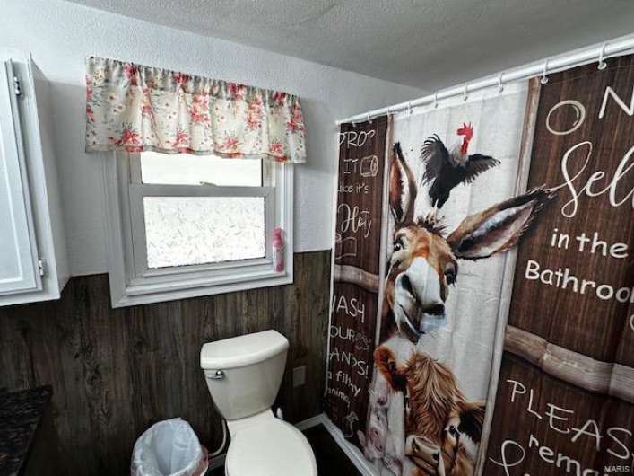 Bathroom featuring wood walls, a textured ceiling, and toilet