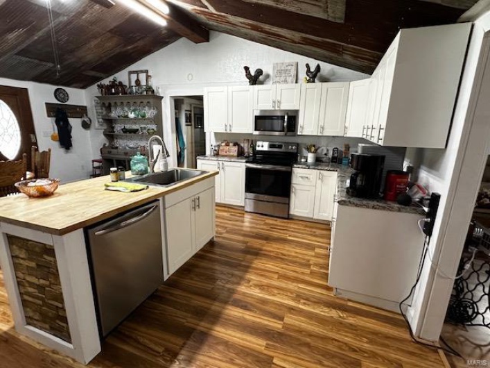 Kitchen with vaulted ceiling with beams, white cabinets, sink, stainless steel appliances, and dark hardwood / wood-style floors