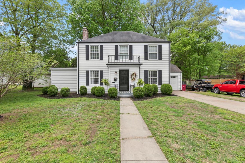 Colonial house featuring a front lawn, driveway, a chimney, and a balcony