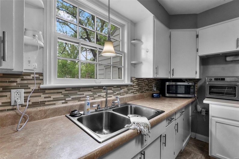 Kitchen featuring tasteful backsplash, a sink, light countertops, stainless steel microwave, and white cabinetry