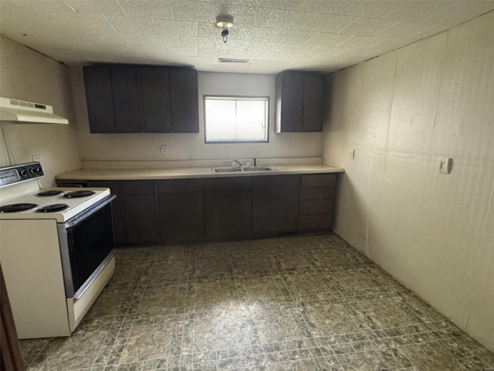 Kitchen featuring white electric stove, under cabinet range hood, light countertops, visible vents, and a sink