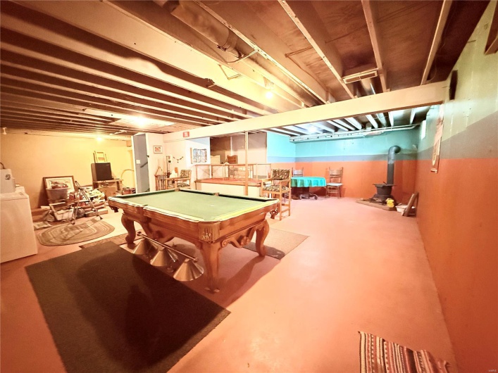 Recreation room featuring concrete flooring, washer / dryer, a wood stove, and pool table
