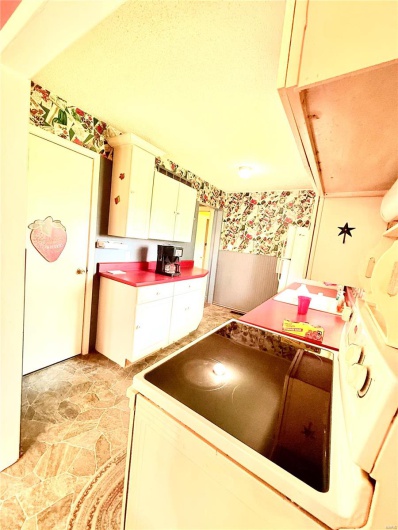 Kitchen featuring white range with electric cooktop, stone finish flooring, wallpapered walls, and white cabinets