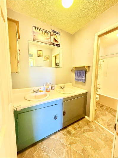 Bathroom with a sink, a textured ceiling, double vanity, and toilet