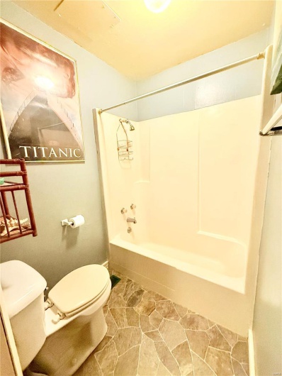 Full bath with toilet, stone finish floor, and  shower combination