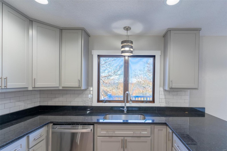 Kitchen with sink, stainless steel dishwasher, dark stone countertops, tasteful backsplash, and decorative light fixtures