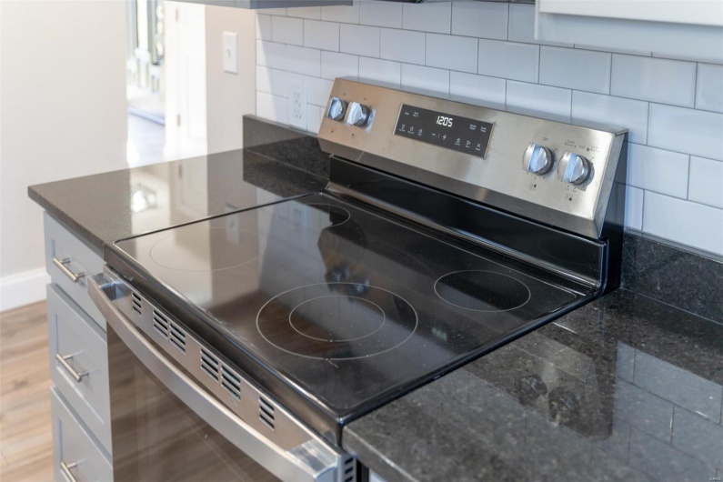 Kitchen featuring decorative backsplash, wood-style flooring, and stainless steel electric range