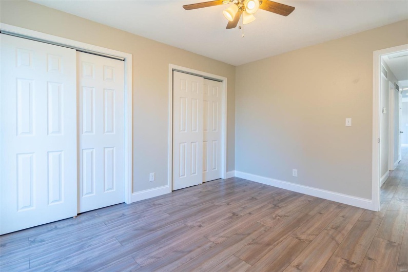 Unfurnished bedroom featuring ceiling fan, two closets, and light wood-style flooring