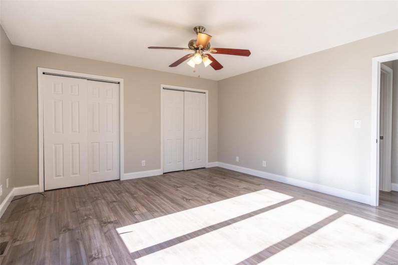 Unfurnished bedroom with ceiling fan, light  wood-style floors, and two closets