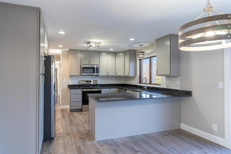 Kitchen with  wood-style floors, decorative light fixtures, kitchen peninsula, and stainless steel appliances