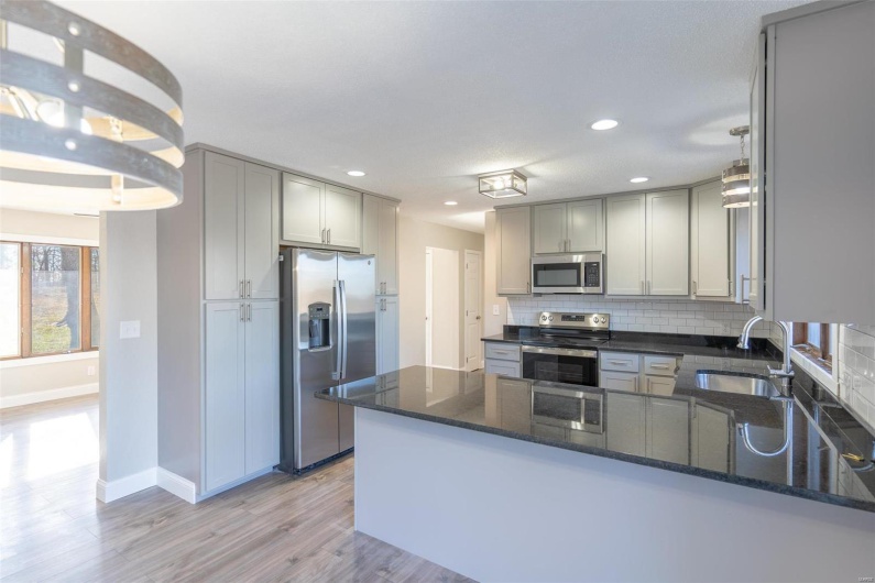 Kitchen with sink, stainless steel appliances, kitchen peninsula, dark stone countertops, and light  / wood-style floors