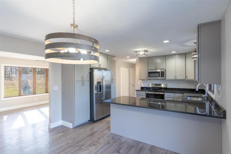 Kitchen with kitchen peninsula, appliances with stainless steel finishes, light wood-type flooring, sink, and hanging light fixtures