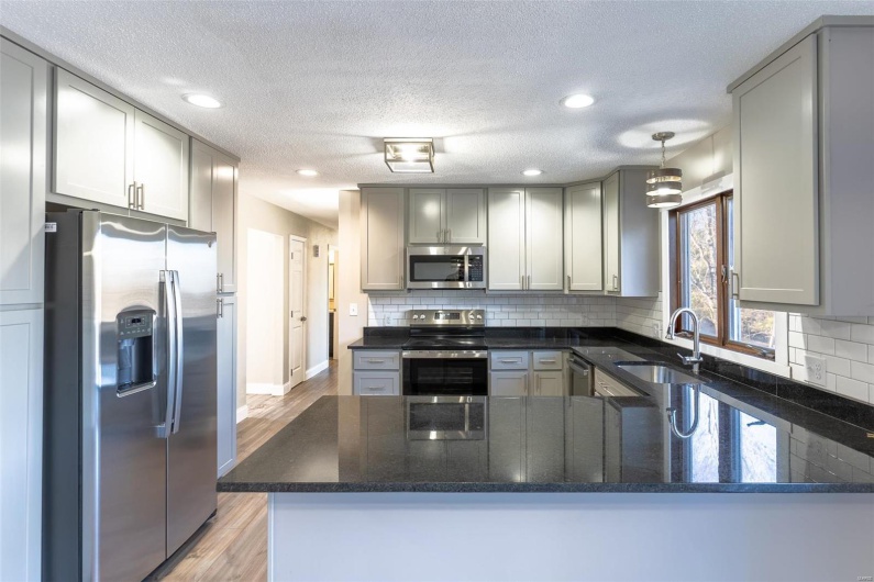 Kitchen with sink, light hardwood / wood-style flooring, kitchen peninsula, decorative light fixtures, and appliances with stainless steel finishes