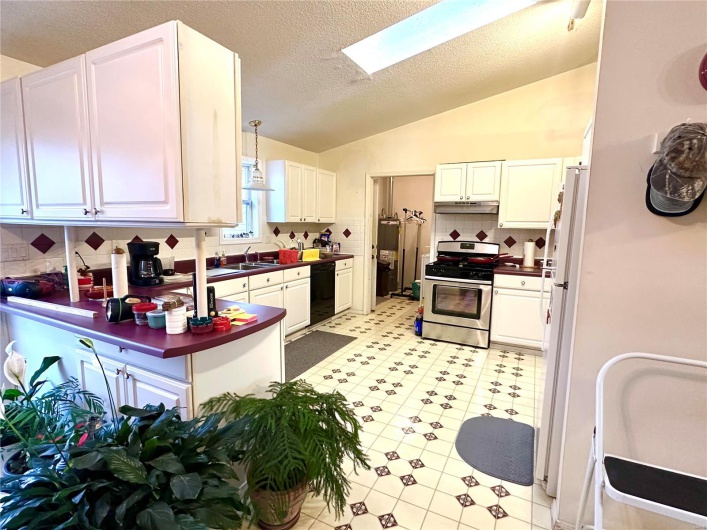 Kitchen featuring black dishwasher, a sink, vaulted ceiling with skylight, under cabinet range hood, and stainless steel gas range oven