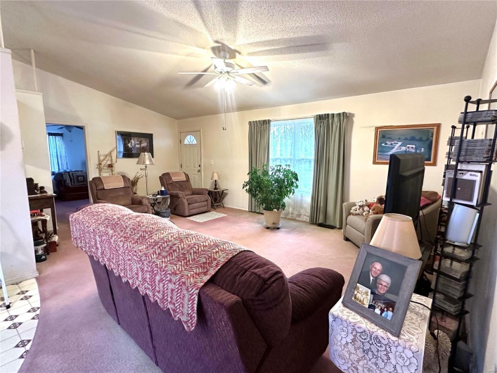Carpeted living room featuring a ceiling fan, vaulted ceiling, and a textured ceiling