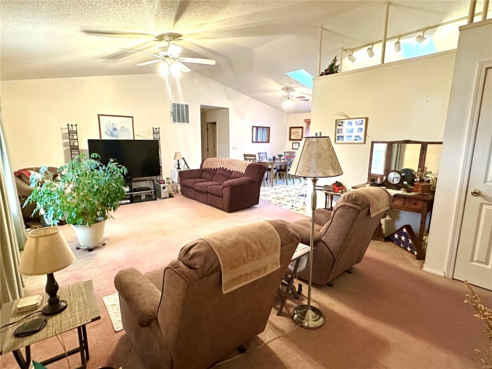 Carpeted living area featuring visible vents, a ceiling fan, lofted ceiling, a textured ceiling, and track lighting