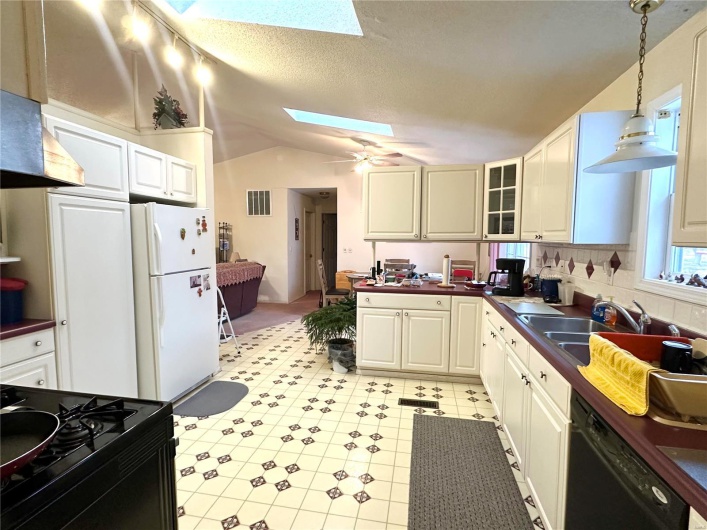 Kitchen featuring pendant lighting, dark countertops, visible vents, vaulted ceiling with skylight, and black appliances