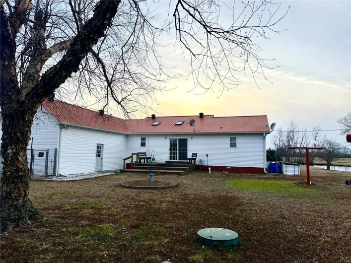 Back of property at dusk with metal roof, a wooden deck, and a lawn