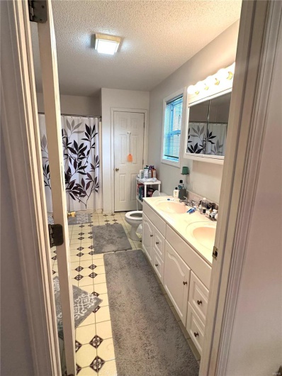 Full bath with double vanity, a textured ceiling, toilet, and a sink