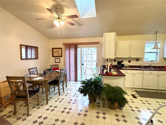 Kitchen with vaulted ceiling with skylight, a ceiling fan, a textured ceiling, white cabinetry, and a sink