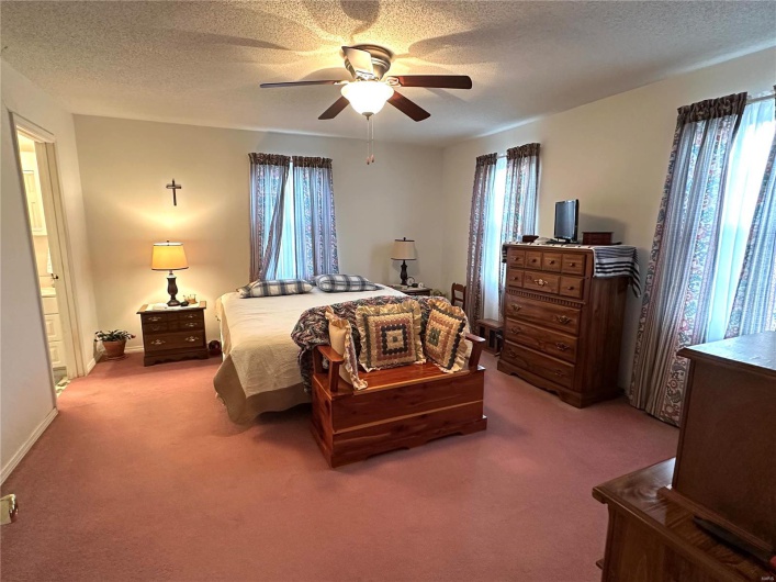 Carpeted bedroom featuring a textured ceiling, multiple windows, and a ceiling fan