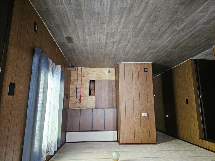 Empty room with wood walls, wood finished floors, and visible vents