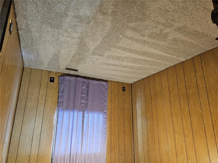 Carpeted empty room with visible vents and wood walls