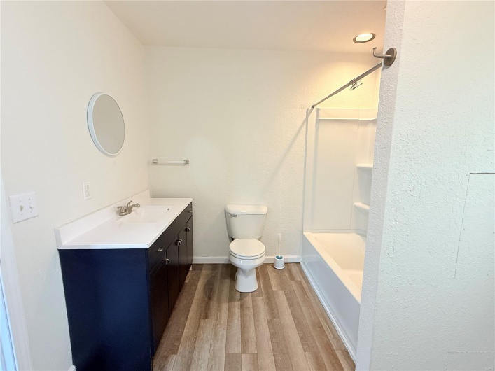 Bathroom featuring wood finished floors, shower / bathtub combination, toilet, vanity, and baseboards