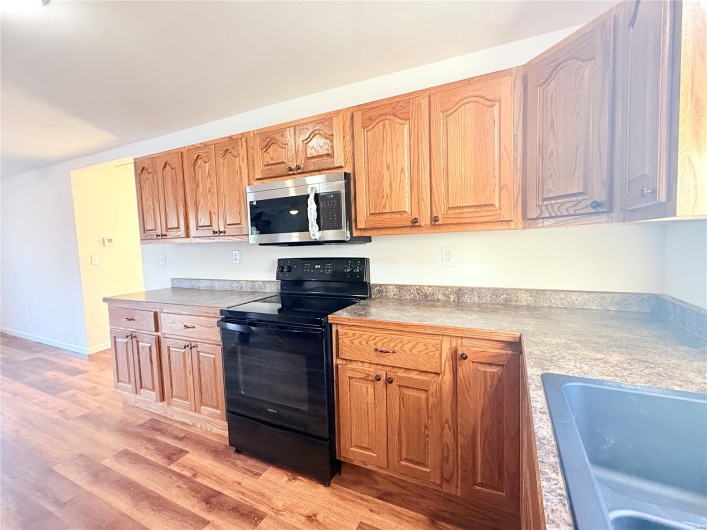 Kitchen with stainless steel microwave, light wood finished floors, black / electric stove, and a sink