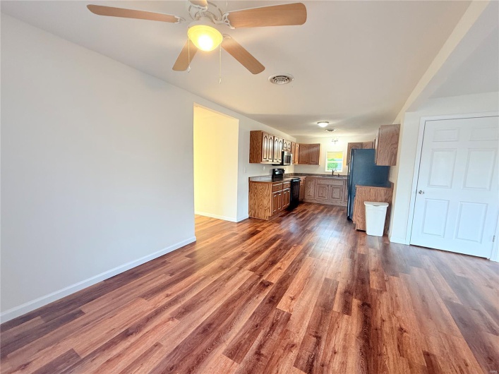 Unfurnished living room with visible vents, baseboards, dark wood-style floors, and ceiling fan