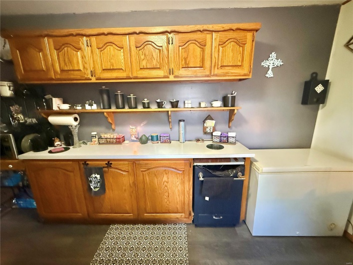 Kitchen with brown cabinets, concrete floors, open shelves, and light countertops