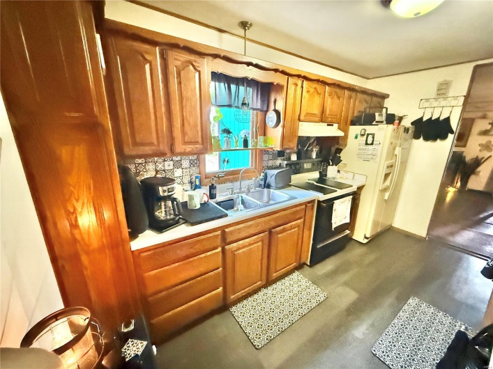 Kitchen with range with electric cooktop, under cabinet range hood, light countertops, a sink, and white refrigerator with ice dispenser