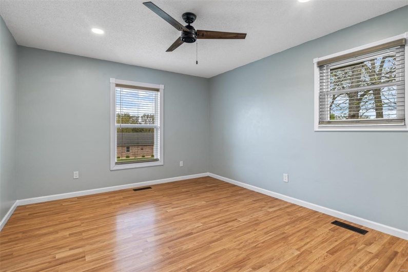 Empty room with light wood-style floors, visible vents, a ceiling fan, and baseboards