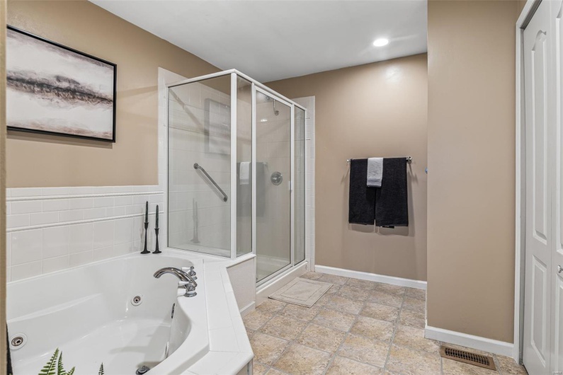 Full bathroom with a stall shower, stone tile flooring, a whirlpool tub, baseboards, and visible vents