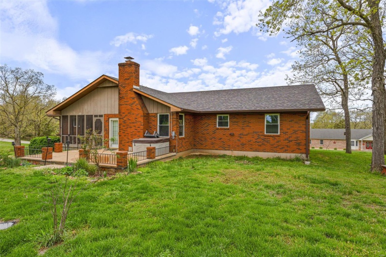 Rear view of house featuring brick siding, a sunroom, roof with shingles, and a lawn
