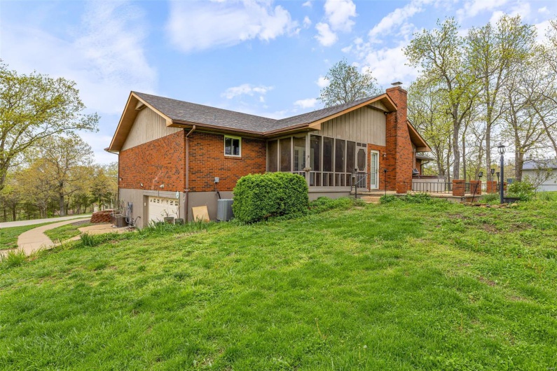 Rear view of property featuring a chimney, an attached garage, a sunroom, and a yard