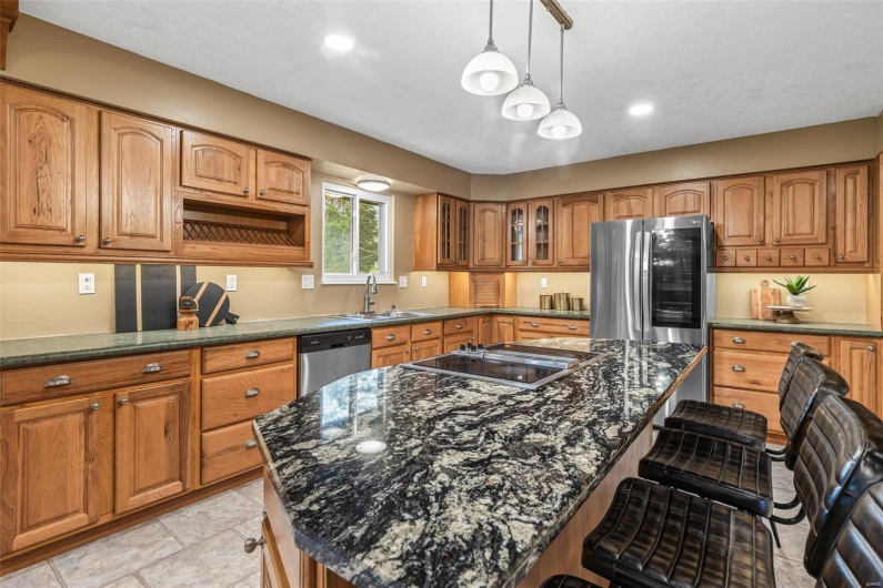 Kitchen with a kitchen breakfast bar, a sink, brown cabinetry, glass insert cabinets, and appliances with stainless steel finishes