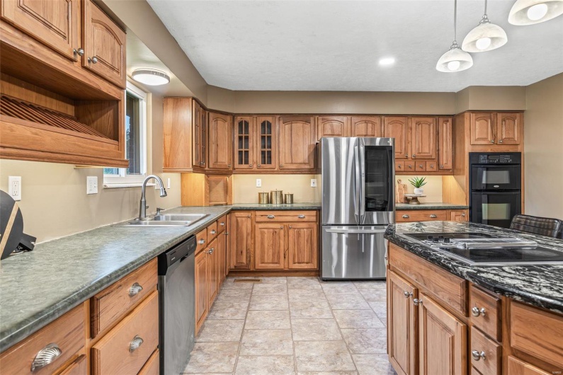 Kitchen with dark countertops, open shelves, a sink, black appliances, and brown cabinets