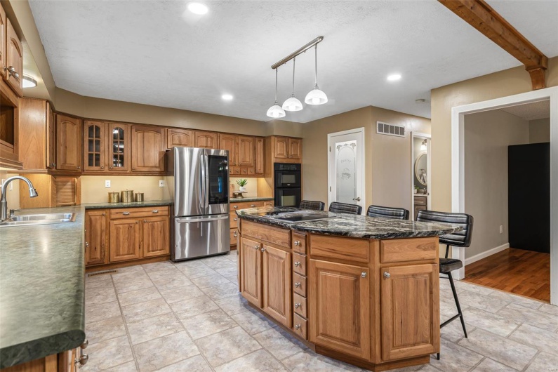 Kitchen with smart refrigerator, dobule oven black, a sink, brown cabinetry, and visible vents