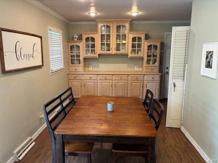 Dining area with dark wood finished floors, baseboards, crown molding, and visible vents