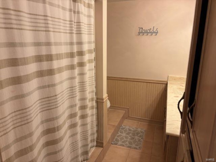 Full bath featuring wainscoting, tile patterned floors, vanity, and toilet