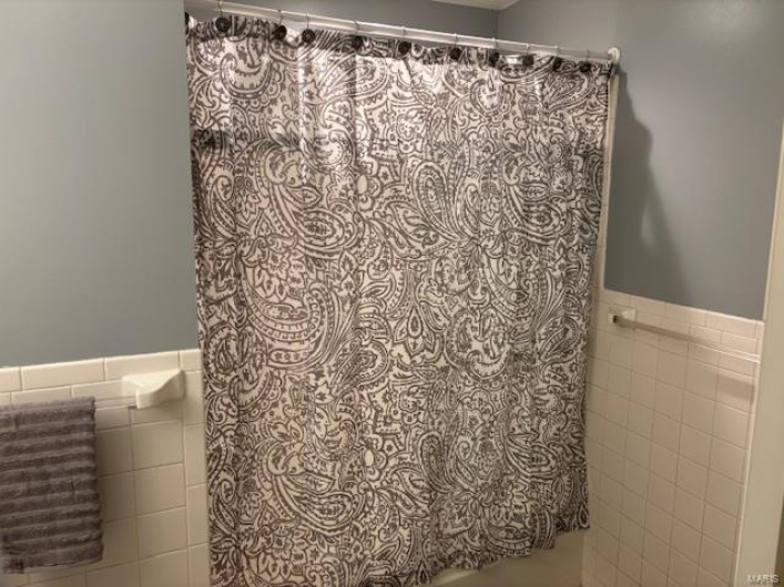 Full bathroom featuring a wainscoted wall, a shower with shower curtain, and tile walls