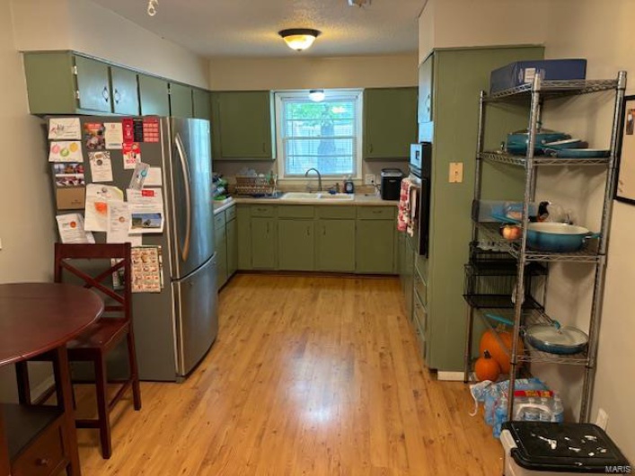 Kitchen with stainless steel fridge, green cabinets, sink, and light hardwood / wood-style floors