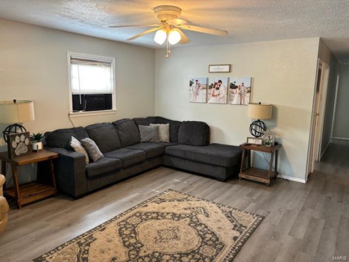 Living room with ceiling fan, a textured ceiling, and hardwood / wood-style floors