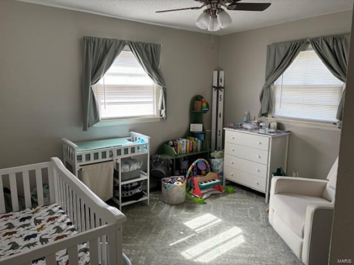 Carpeted bedroom with ceiling fan and a crib