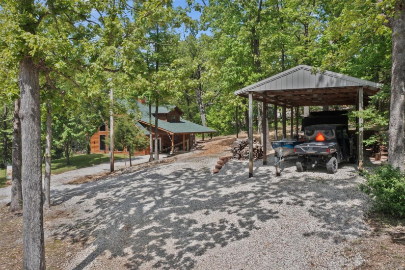 View of patio / terrace featuring a detached carport, gravel driveway, and view of wooded area