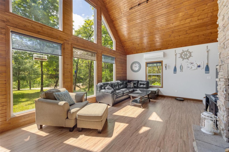 Living room featuring high vaulted ceiling, a wall unit AC, healthy amount of natural light, wooden ceiling, and a wood stove