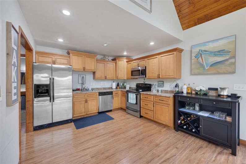 Kitchen with appliances with stainless steel finishes, light wood-type flooring, recessed lighting, light stone counters, and lofted ceiling