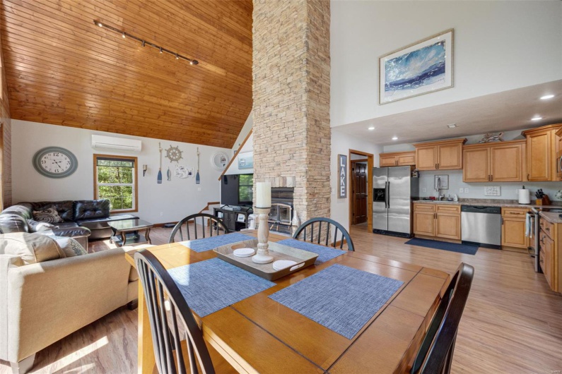 Dining room with an AC wall unit, high vaulted ceiling, rail lighting, light wood-style flooring, and a stone fireplace