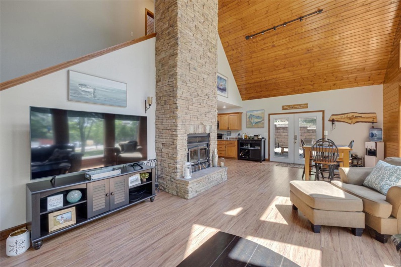 Living area with high vaulted ceiling, a fireplace, light wood-type flooring, rail lighting, and french doors